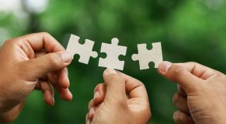 Drie handen houden elks een puzzelstuk vast