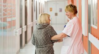 Verpleegkundige geriatrie en patiënt wandelen hand in hand door de zorgeenheid AZ Sint-Maarten
